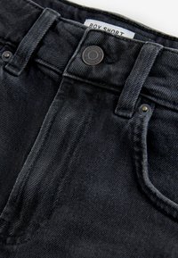 Svarta denimshorts med en lätt textur, en midja med en metallknapp och fickor fram. Etiketten säger "BOX SHORT."
