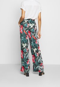 Luchtige zwarte broek met grote rode en witte bloemenprint. Heeft een elastische taille en wijde pijpen, gecombineerd met een loszittend wit bovenstuk.