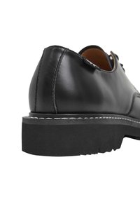Scarpa di pelle nera con punta rotonda, impreziosita da cuciture bianche lungo la suola e una suola in gomma nera spessa e texturizzata.