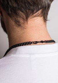 Must mustraed aheliga kett, millel on omavahel ühendatud lingid, varustatud homaariklamberiga ja kaunistustega taga, kantud valge särgi peal.