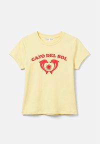 T-shirt jaune à manches courtes avec texte rouge "CAYO DEL SOL" au-dessus de deux dauphins formant un cœur autour d'un dessin de soleil.