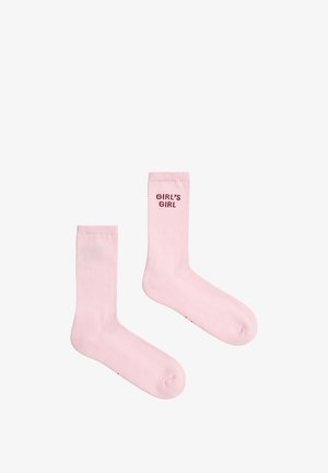 Lyserøde crew-længde sokker med ribbet struktur, en sok viser teksten "GIRL'S GIRL" nær den øverste kant i mørkerøde bogstaver.
