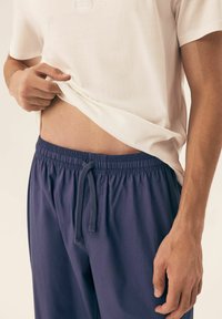 Lightweight white t-shirt with short sleeves, paired with navy blue elasticized shorts featuring a drawstring and smooth texture.