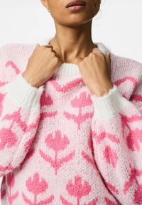 Maglione lavorato a maglia in rosa e bianco, con un motivo floreale, texture morbida, scollatura ampia e polsini a coste. Tessuto leggero e caldo.