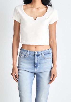 Bílý pruhovaný crop top s výstřihem do V a krátkými rukávy, nošený s světle modrými džíny s vysokým pasem a knoflíkovým zapínáním.