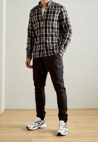 Zwart-wit geruit shirt, met knopen en lange mouwen; zwarte cargo broek met zijzakken; witte sportieve schoenen met grijze accenten.