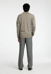 Svetlo rjav pleten pulover s okroglim izrezom, v kombinaciji z sivimi hlačami viskega pasu z ravnim krojem in gladko površino.