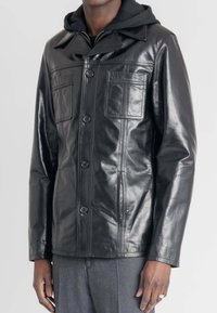 Zwarte leren jack met een knopenfront, twee borstzakken, kraag en aangehechte zwarte hoodie. Soepele textuur met zichtbare naden.