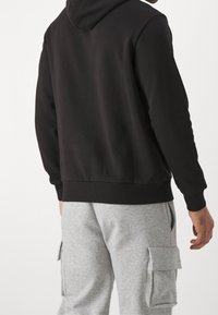Sweatshirt à capuche noir avec un ourlet et des poignets côtelés, vu de dos, associé à un pantalon cargo gris avec des poches latérales.