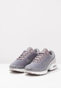 Baskets Nike en dégradé de gris, avec un dessus en daim lisse, une pointe arrondie et une semelle blanche avec un amorti visible. Lacets gris et logo.
