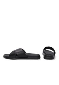 Zwarte slidensandalen met een glad leren bovenwerk, voorzien van gekruiste banden en een platte rubberen zool. Minimalistisch ontwerp zonder versieringen.