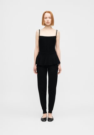 Top negro de estilo peplum con textura acanalada vertical y tirantes finos, combinado con pantalones negros ajustados y zapatillas negras simples. Fondo plano.