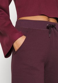 Suéter corto burdeos con mangas acampanadas combinado con joggers burdeos a juego. Los joggers cuentan con cintura con cordón y bolsillos laterales.