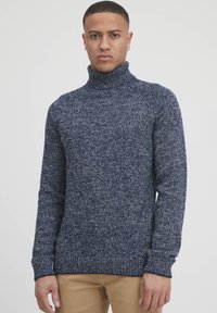 Navy modra pletena turtleneck pulover s teksturiranim, pikastim vzorcem in rebrastimi manšetami. Prilega se telesu in ima dolge rokave.