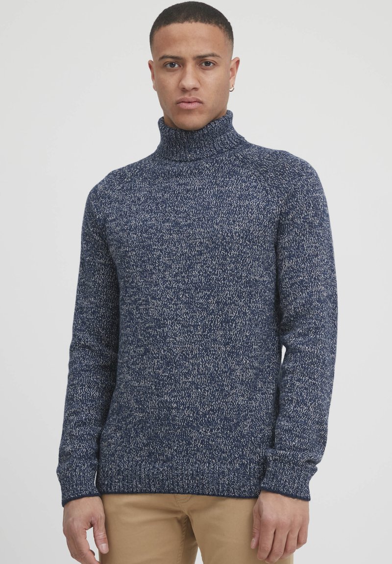 Navy modra pletena turtleneck pulover s teksturiranim, pikastim vzorcem in rebrastimi manšetami. Prilega se telesu in ima dolge rokave.