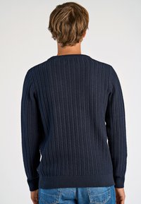 Marineblauer Strickpullover mit geripptem Muster, rundem Halsausschnitt und langen Ärmeln. Verfügt über einen enganliegenden Saum und seitliche Details.