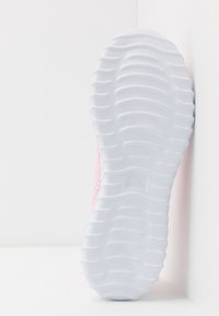 Světle růžová atletická bota s texturovaným svrškem a flexibilní bílou gumovou podrážkou, která má zvlněný vzor pro lepší přilnavost.