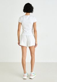 Witte aansluitende t-shirt en witte shorts met oogjeskant, gecombineerd met multikleurige sportieve sneakers. Zachte katoen en gestructureerde stof.