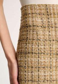 Jupe tissée en tweed beige avec un motif à carreaux, mettant en valeur des accents blancs et verts, et une finition texturée.