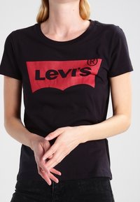 Czarna bawełniana koszulka z okrągłym dekoltem i krótkimi rękawami. Na przodzie znajduje się duże czerwone logo Levi's. Miękka struktura.
