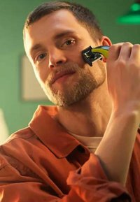 Rasoio elettrico con un design nero e verde, tenuto contro un volto con una leggera barba. Lo sfondo presenta un colore verde tenue.