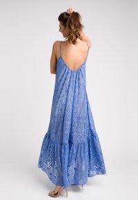 Sukienka maxi w jasnoniebieskim kolorze z przezroczystym, okrągłym wzorem, ramiączkami na spaghetti i niskim plecami. Posiada wielowarstwowy falbaniasty dół i jest lekka.