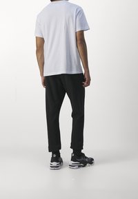 Weißes Baumwoll-T-Shirt mit kurzen Ärmeln, kombiniert mit schwarzen Jogginghosen und schwarzen Sneakern mit weißen Sohlen und Akzenten.