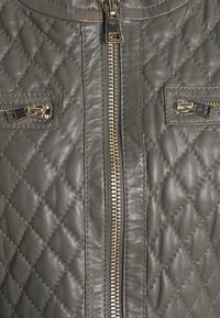 Prošívaná kožená bunda v šedé barvě se zlatými zipy a dvěma předními kapsami. Má centrální zapínání na zip a hladkou texturu.