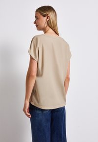 Beige Bluse mit kurzen Ärmeln, glatter Textur und rundem Ausschnitt, kombiniert mit blauen Jeans mit weiter Beinform.