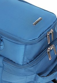 Modrý látkový batoh s hladkou texturou, dvojitými zipovými oddíly a metalickým logem na vrchu.