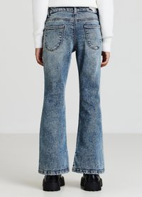 Jeans in denim azzurro svasati con un lavaggio sbiadito, caratterizzati da due tasche posteriori e un orlo cucito, abbinati a stivali neri con suola spessa.