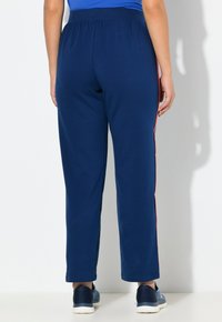 Marineblauwe broek met een losse pasvorm, voorzien van rode zijstrepen. Gemaakt van zachte stof met een elastische tailleband voor comfort.