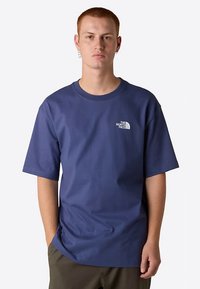 Mörkblå bomulls-t-shirt med korta ärmar, rund halsringning och vit logotyp på vänster bröst. Slät textur, avslappnad passform.