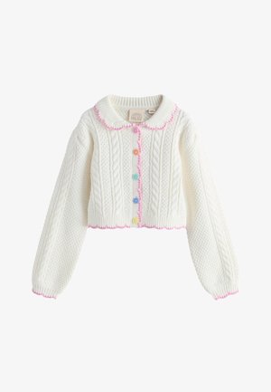 Main d'enfant portant une manche en maille blanche avec bordure rose à côté d'une jupe en tulle superposée multicolore dans des tons roses, violets et jaunes.