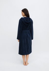 Μπλε ναυτικό μπουρνούζι από απαλό, υφασμάτινο ύφασμα με υφή, με κουκούλα, μακριά μανίκια και δετή ζώνη στη μέση, που φτάνει μέχρι το μέσο της γάμπας.