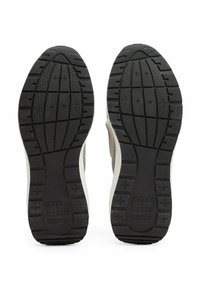 Soli delle sneaker con gomma nera testurizzata, un motivo di battistrada, accenti grigio chiaro e branding visibile nella zona del tallone.