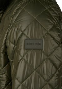 Olijfgroene gewatteerde jas met diamanten stiksel en rechthoekige patch met het label "HECHTER" op het schoudergebied.