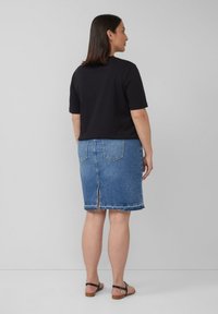 Schwarzes kurzärmeliges Oberteil, kombiniert mit einem blauen Jeans-Bleistiftrock mit fransigem Saum und einem Rückenschlitz, getragen mit schwarzen Sandalen mit Knöchelriemen.