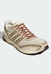 Μπεζ αθλητικό παπούτσι με επάνω μέρος από δίχτυ, καφέ λεπτομέρειες και κορδόνια. Διαθέτει σχέδιο με τρεις ρίγες, μαλακό πάτο και υφή για καλύτερη πρόσφυση.