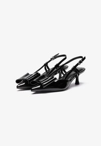 Decolté in vernice nera con punta affilata, accenti decorativi a forma di fiocco e tacco kitten di 5 cm. Incluse cinture regolabili alla caviglia.