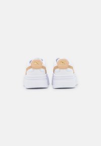 Baskets blanches à plateforme avec des accents beige, présentant une forme arrondie et un panneau arrière texturé. Détail du logo jaune sur le talon.