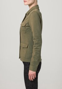 Olive green shirt jacket with a collar, long sleeves, and two chest pockets. Made from a soft, textured fabric.