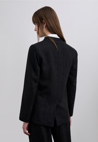 Sort blazerkjole med nålestriber lavet af tekstureret stof, der har en skræddersyet pasform, revers med hakket slag og en slids midt på ryggen. Subtile shimmer-detaljer.