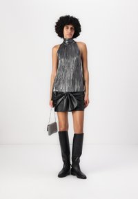 Top halter metálico con rayas verticales, minifalda negra de cuero sintético con detalle de lazo, botas negras hasta la rodilla y un pequeño bolso metálico.