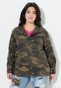 Giacca mimetica in verde e marrone realizzata in un tessuto leggero, con chiusura a scatti, due tasche frontali e colletto. Indossata sopra una maglietta rosa.