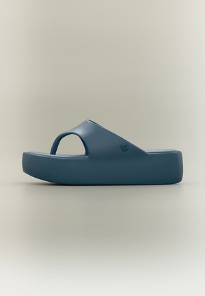 Une sandale slide bleu foncé avec une semelle épaisse et une large bride, vue de côté sur un fond neutre.