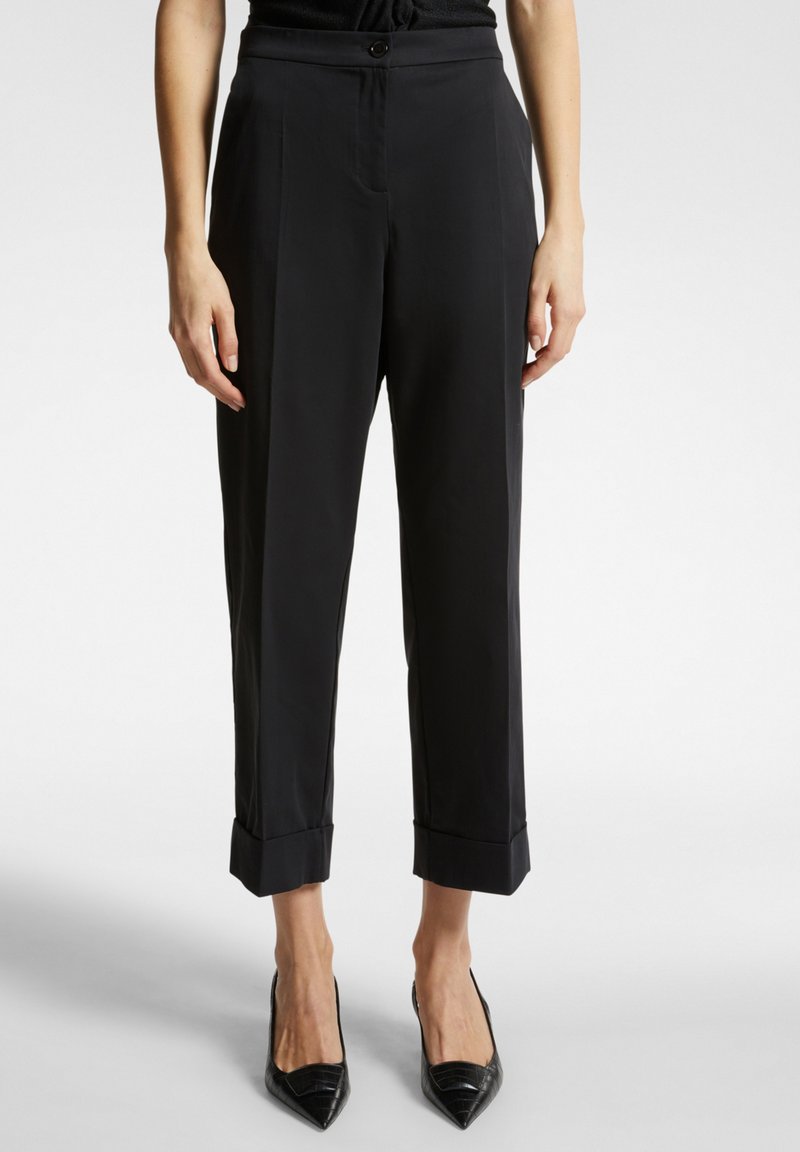 Pantaloni neri con un fit su misura, dotati di chiusura con bottone, tasche laterali e orli arrotolati. Tessuto liscio con una leggera lucentezza.