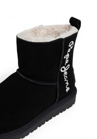 Juodas zomšinės kulkšninių botai su minkštu švelniu pamušalu, su baltu logotipu šone ir tekstūruotu guminiu padu geresniam sukibimui.