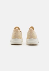 Beige sportsko med strikket mesh-overdel, myk hæltab, og hvit gummisåle, med et strukturert design for pusteevne.