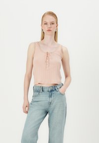 Débardeur rose clair à côtes avec un détail de lien et des boutons au cou; associé à un jean en denim bleu clair déchiré.